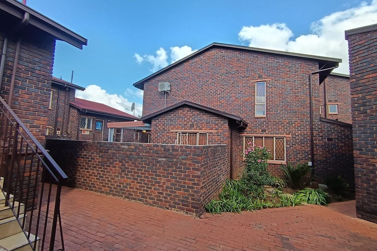 A rear view of a face brick townhouse featuring a private paved courtyard area and secure window fixtures.