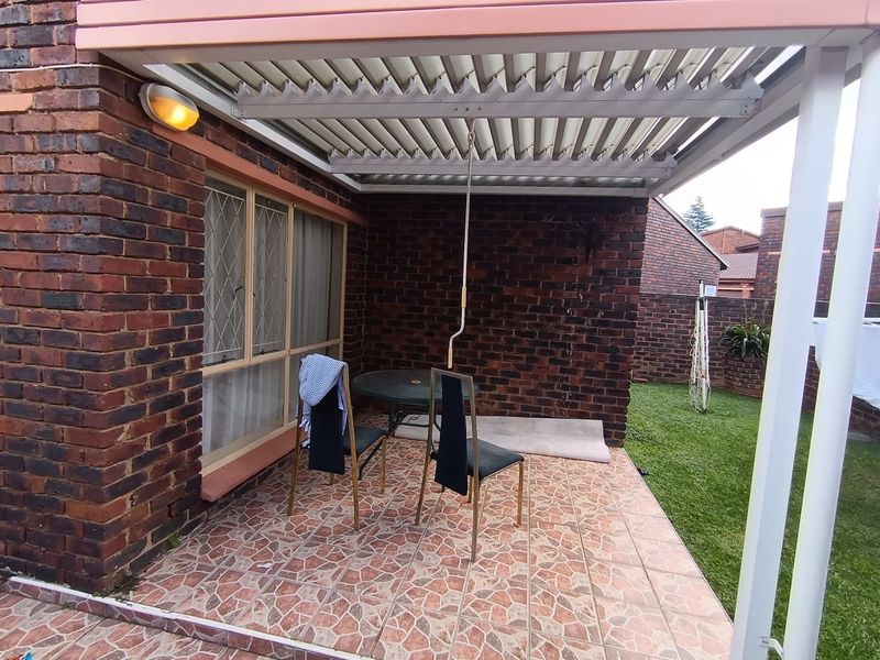 Covered patio area featuring a louvered roof, brick exterior walls, and tiled flooring, overlooking a private garden space.