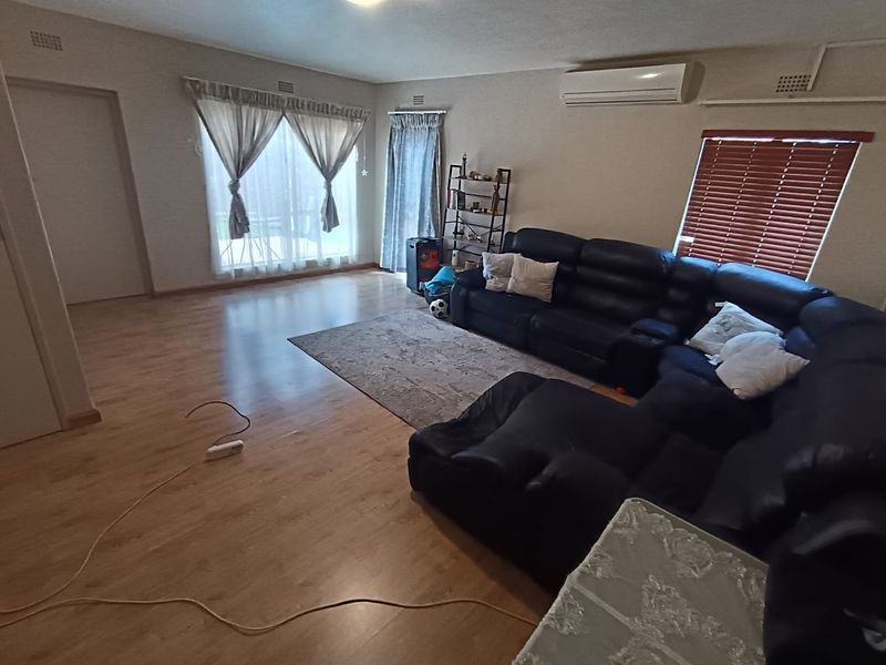 Spacious living room featuring laminate flooring, a wall-mounted split-system air conditioner, and large windows with fitted blinds and curtains.