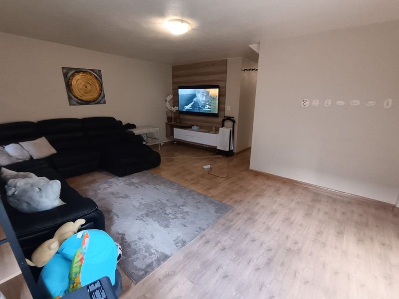 A spacious living room featuring light-toned laminate flooring and a decorative wood-paneled feature wall for the television.