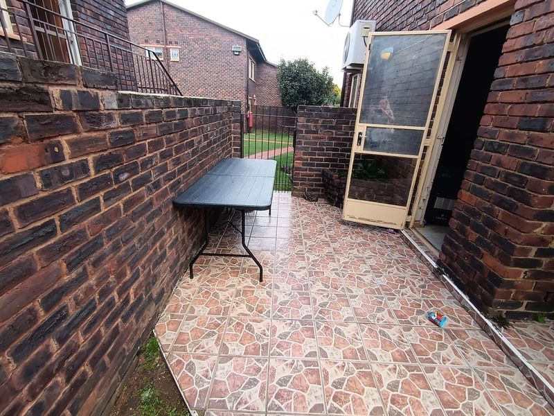 A private outdoor patio area featuring brick walls, tiled flooring, and a security screen door, providing a functional space for outdoor relaxation.