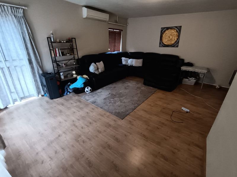 A spacious living room featuring laminate flooring, a wall-mounted air conditioning unit, and access to an outdoor area through a sliding glass door.