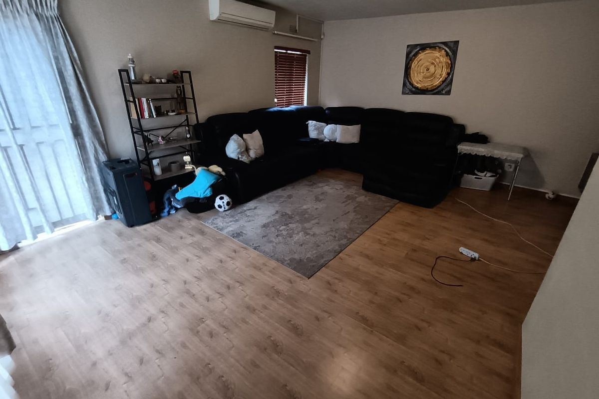 A spacious living room featuring laminate flooring, a wall-mounted air conditioning unit, and access to an outdoor area through a sliding glass door.