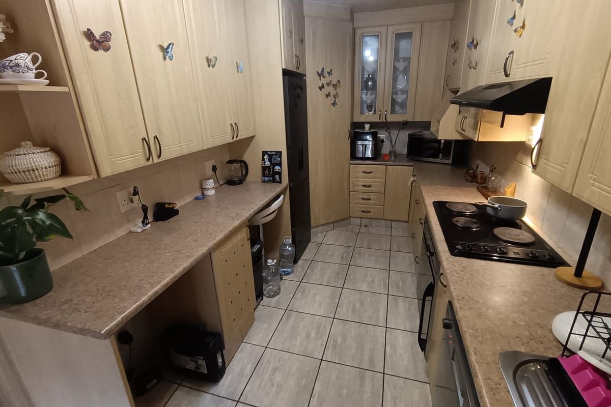 A functional galley-style kitchen featuring laminate cabinetry, ample countertop space, an electric hob with extractor fan, and durable ceramic floor tiling.