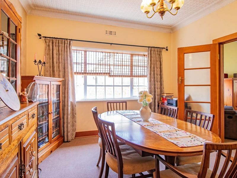 A traditional dining room featuring a classic pressed metal ceiling, timber-framed glass doors, and a large multi-pane window allowing natural light.