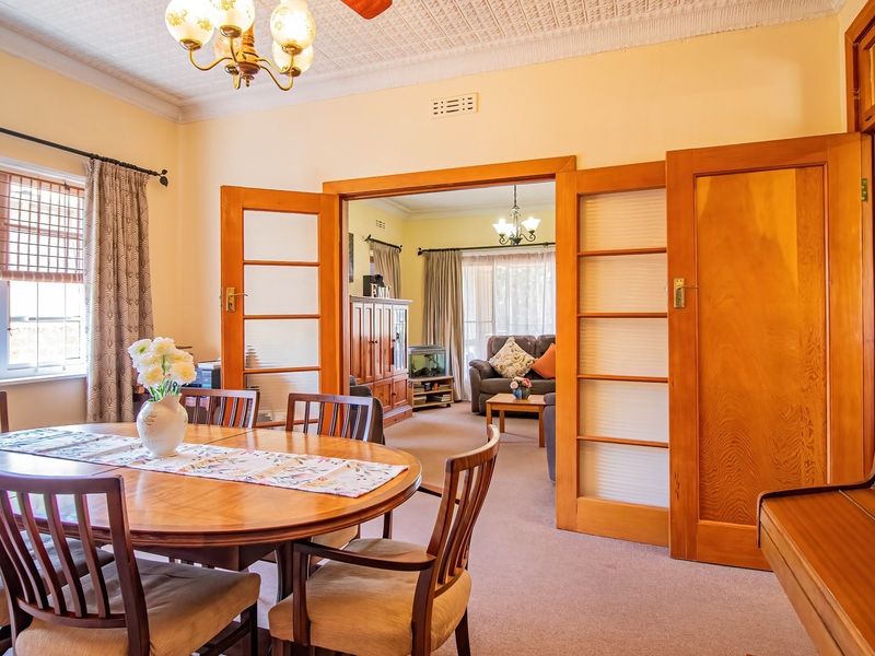 A formal dining room featuring a classic pressed metal ceiling, chandelier lighting, and timber-framed glass sliding doors connecting to the adjacent living area.