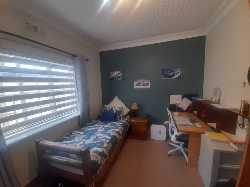 A functional bedroom featuring a textured ceiling, coving, and modern roller blinds, providing a comfortable space with neutral and accent wall finishes.