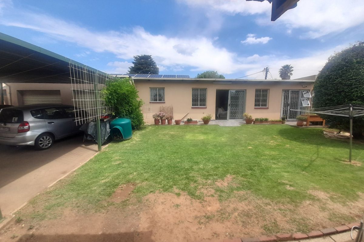 Rear view of the property featuring a lawn, carport, and solar panels installed on the roof.