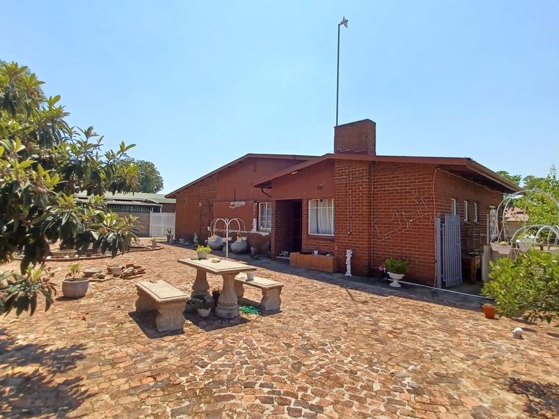 A rear view of a traditional red brick house featuring a large cobblestone patio area and a prominent brick chimney.