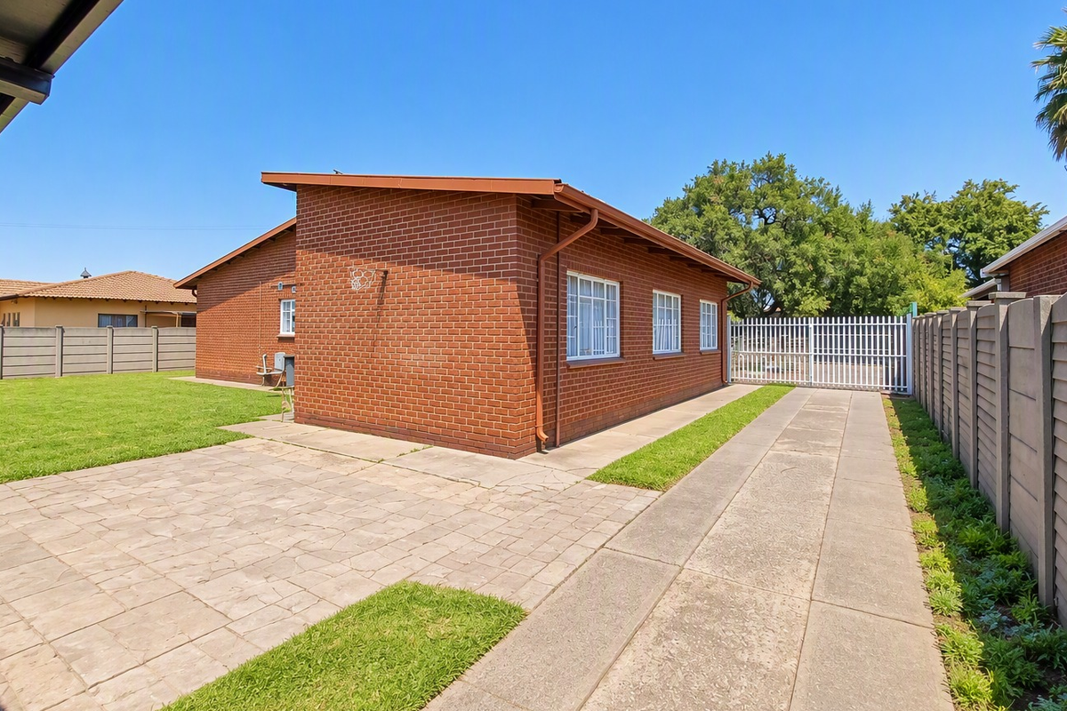 Rear view of the property featuring a face brick exterior, paved driveway, private patio area, and secure perimeter walling with a metal gate.