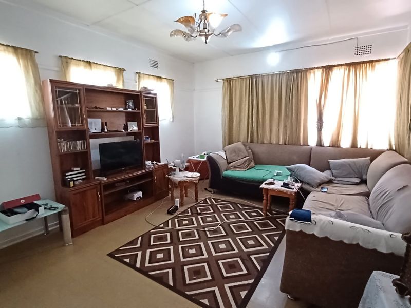 A spacious living room featuring classic ceiling cornices and ventilation grilles, offering a functional layout ready for modern updates and cosmetic improvements.