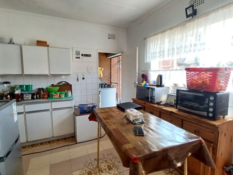 A functional kitchen featuring white built-in cabinetry, tiled splashbacks, and tiled flooring, offering a practical layout with direct access to an adjacent utility area.