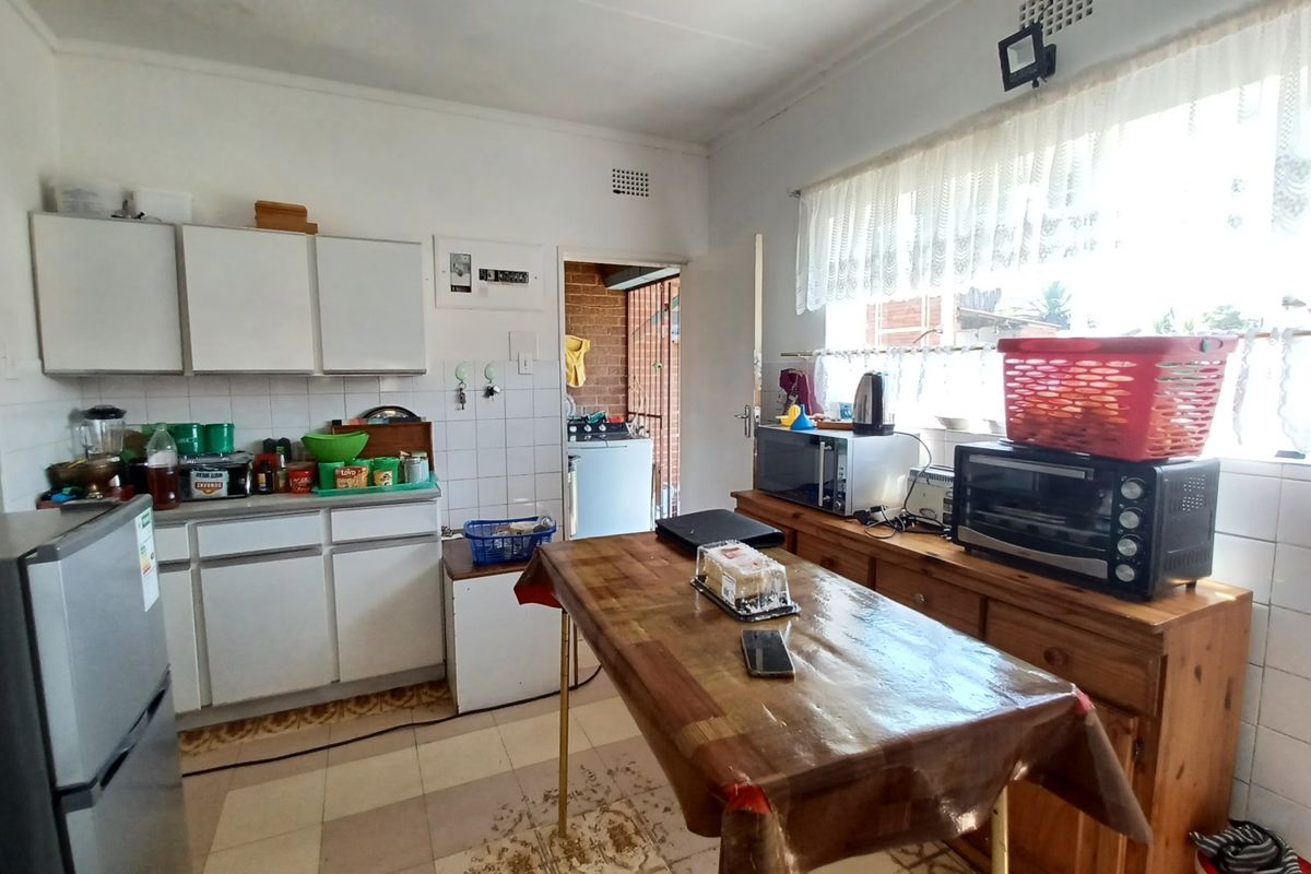 A functional kitchen featuring white built-in cabinetry, tiled splashbacks, and tiled flooring, offering a practical layout with direct access to an adjacent utility area.