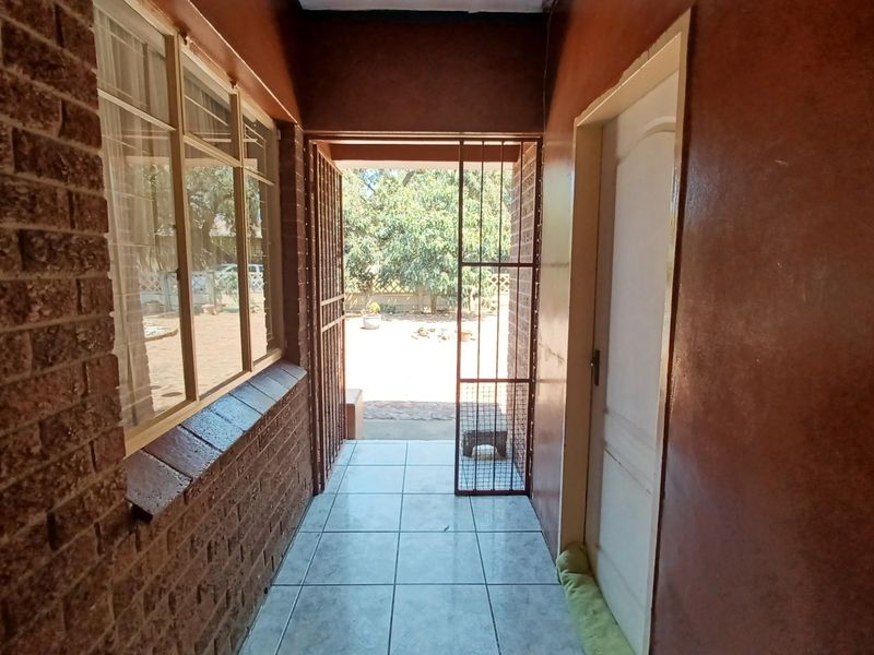 A covered patio area featuring tiled flooring, exposed brickwork, and a security gate leading out to the garden.