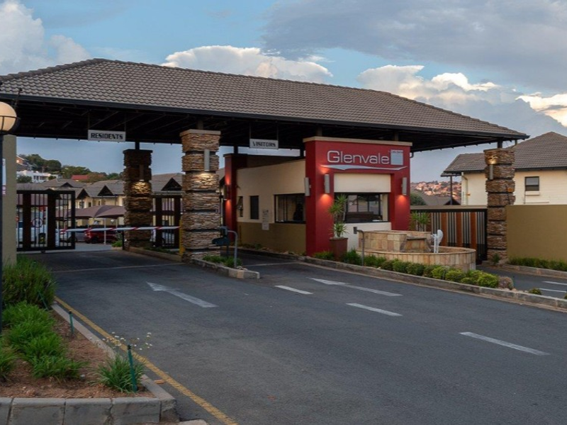 The secure entrance to Glenvale complex featuring a manned gatehouse, boom gate access, stone-clad pillars, and well-maintained landscaping.