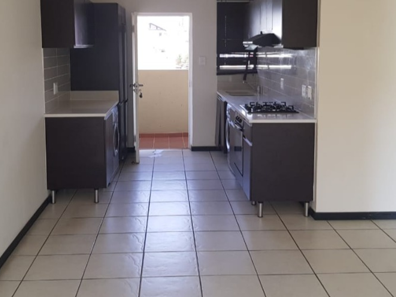 A functional, empty kitchen featuring dark cabinetry, tiled flooring, a gas hob, and an extractor fan, with direct access to an outdoor balcony area.