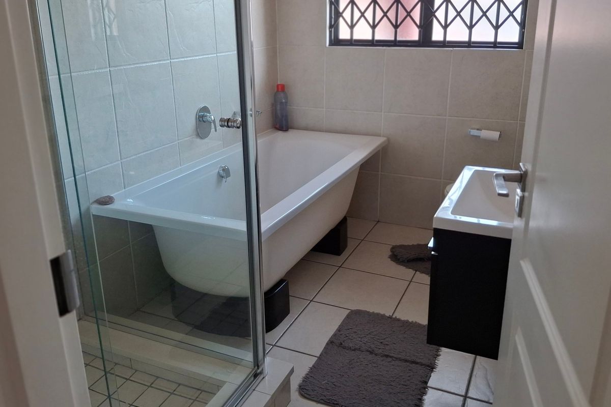 A functional bathroom featuring a freestanding bathtub, a separate glass-enclosed shower, and a wall-mounted basin with tiled finishes throughout.