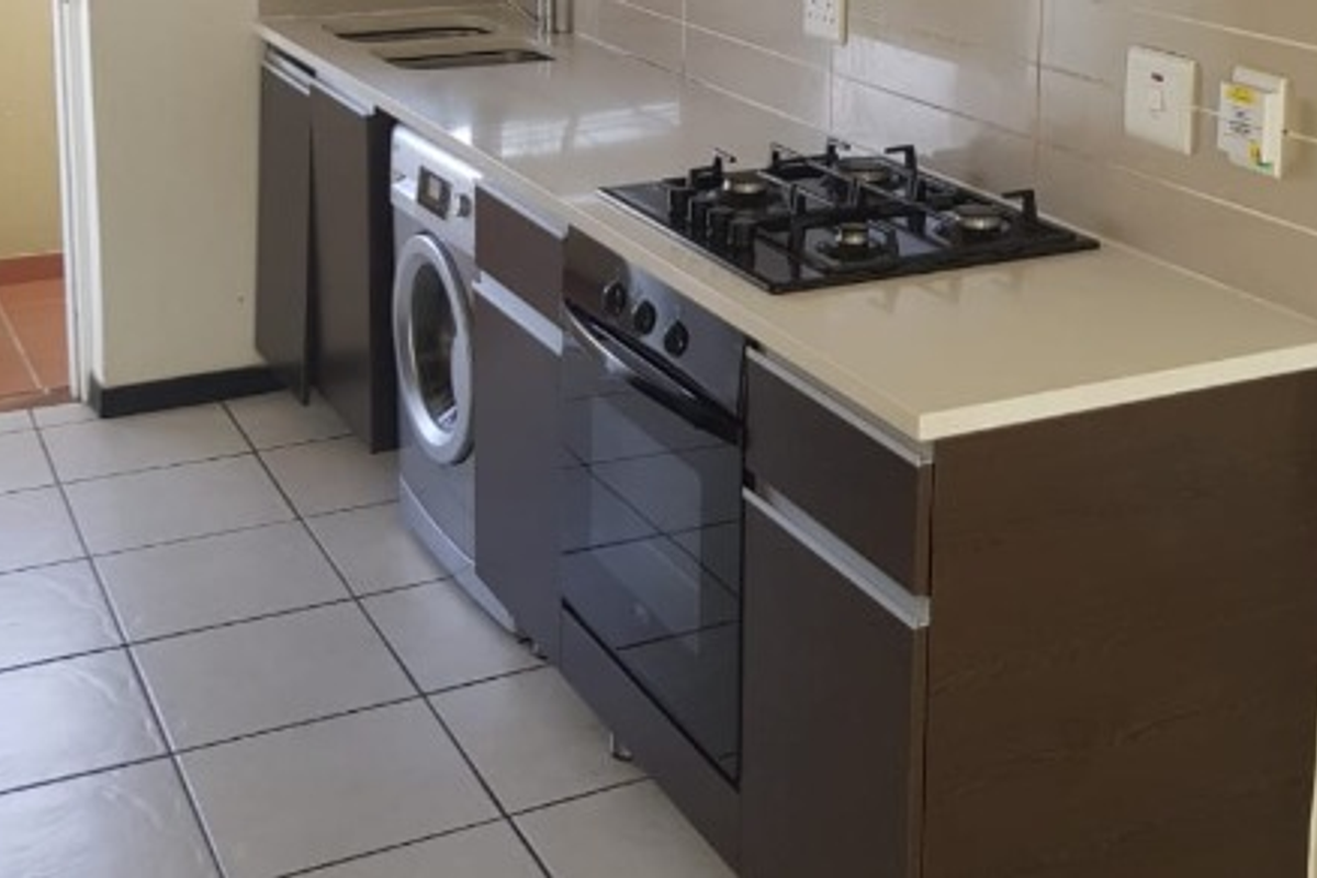 A compact, modern kitchen featuring dark cabinetry, stone countertops, a built-in gas hob, oven, and tiled flooring with direct access to an outdoor area.