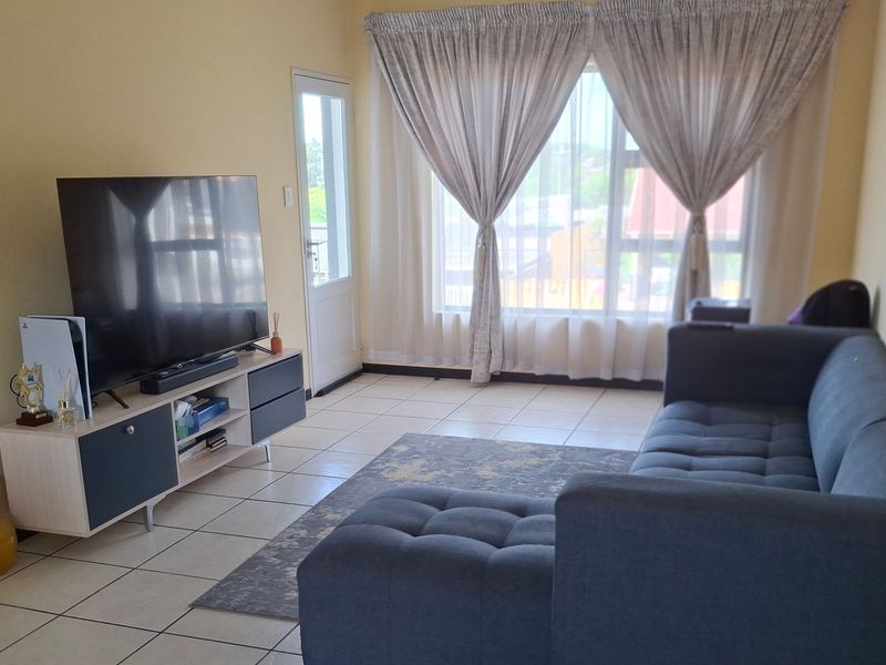 A bright living room featuring tiled flooring, a large window with curtains, and a glass panel door leading to the exterior.