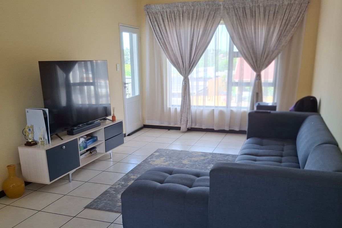 A bright living room featuring tiled flooring, a large window with curtains, and a glass panel door leading to the exterior.