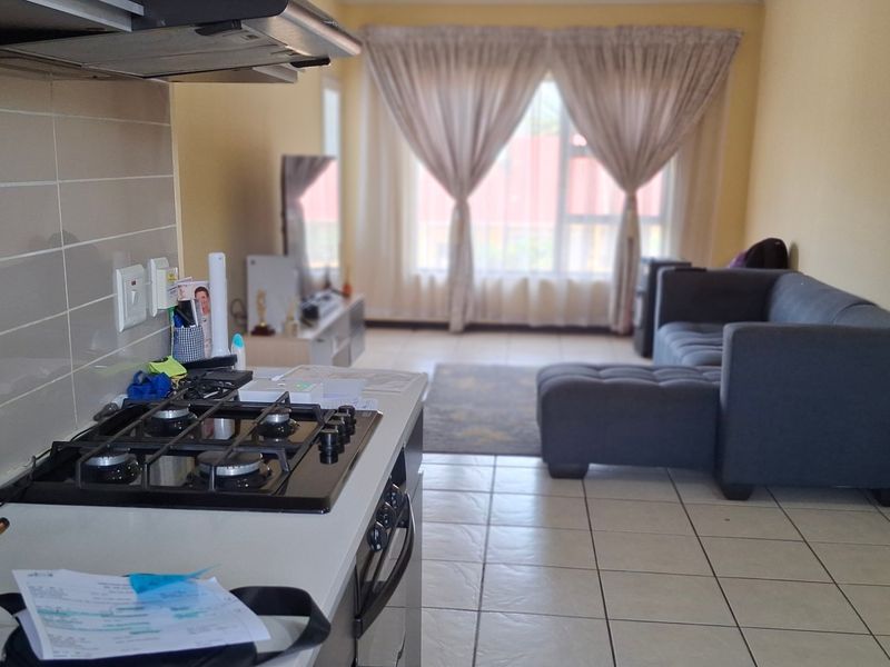 Open plan living area featuring a kitchen with a gas hob and extractor fan, flowing into a comfortable lounge space with tiled flooring.