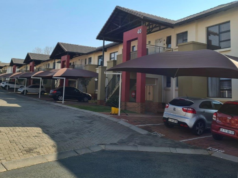 Exterior view of a townhouse complex featuring paved driveways, dedicated shade cloth carports, and multi-level residential units with balconies.