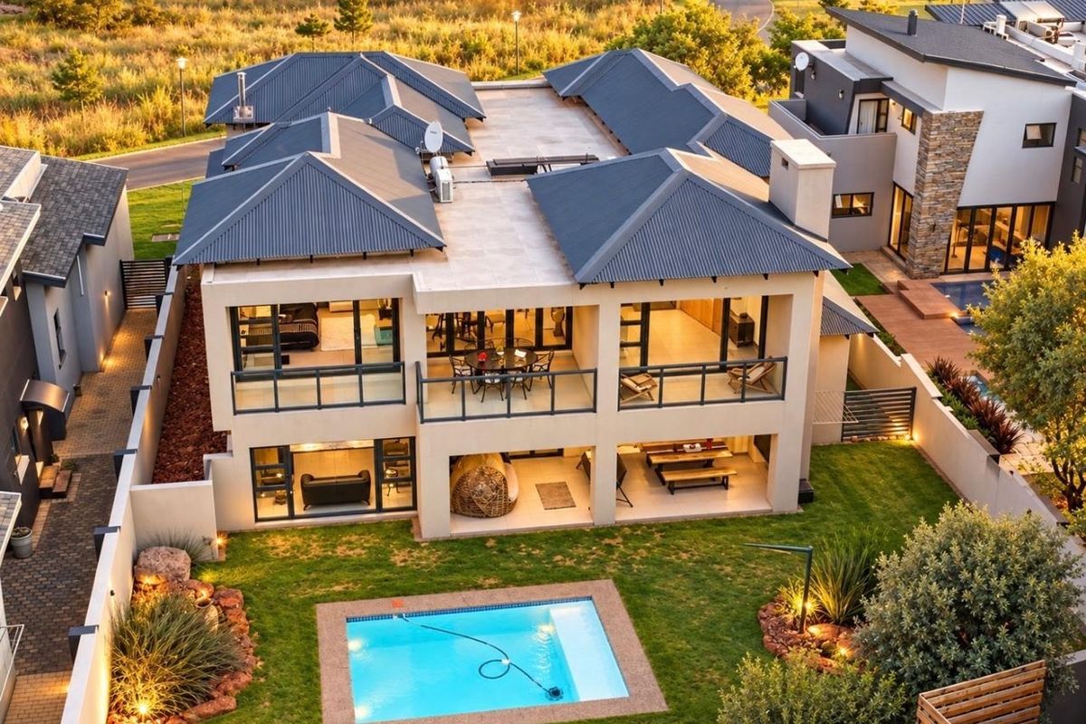 Aerial view of a modern double-story residence featuring a swimming pool, landscaped garden, covered patio, and upper-level balcony with contemporary architectural finishes.
