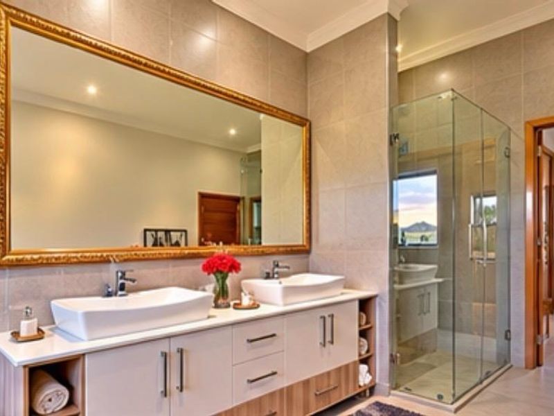 Modern bathroom featuring a double vanity with vessel sinks, large framed mirror, and a spacious glass-enclosed shower with neutral wall tiling.