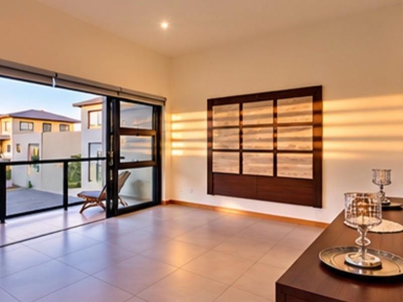 Spacious living area featuring large sliding glass doors leading to a balcony, tiled flooring, and modern built-in wall paneling with warm natural light.