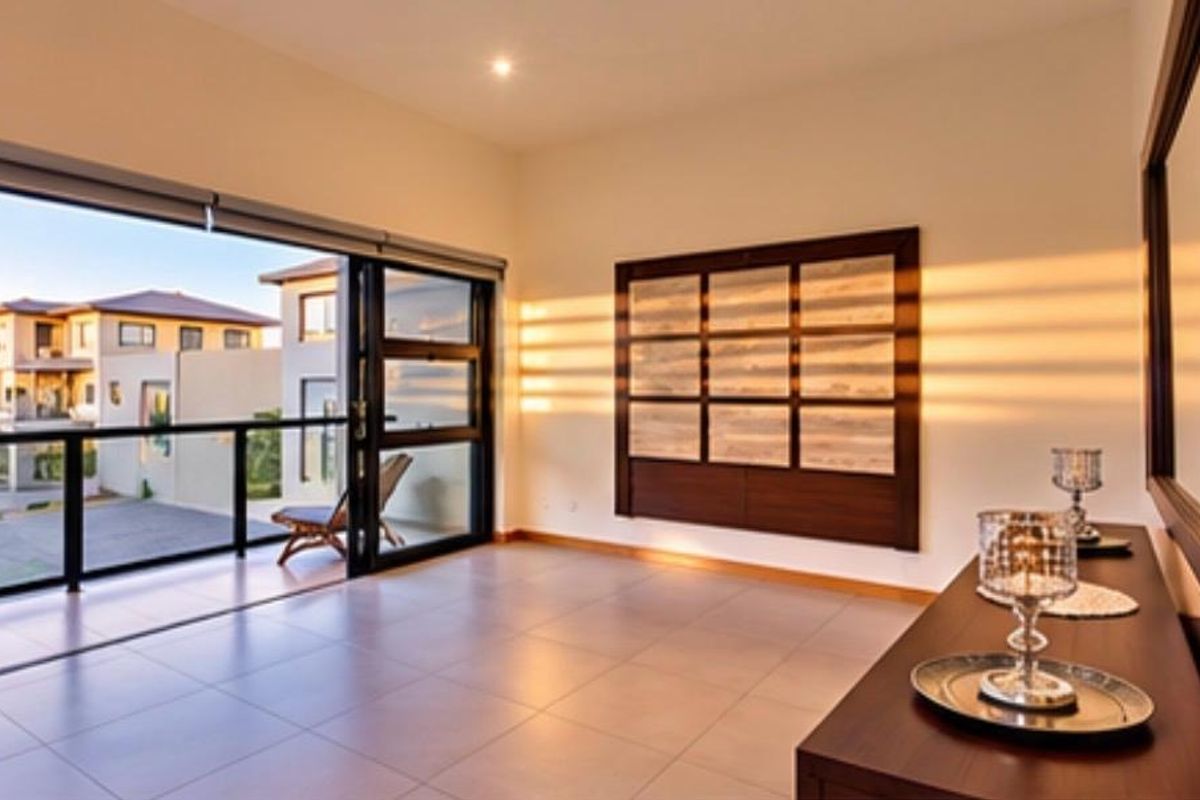 Spacious living area featuring large sliding glass doors leading to a balcony, tiled flooring, and modern built-in wall paneling with warm natural light.