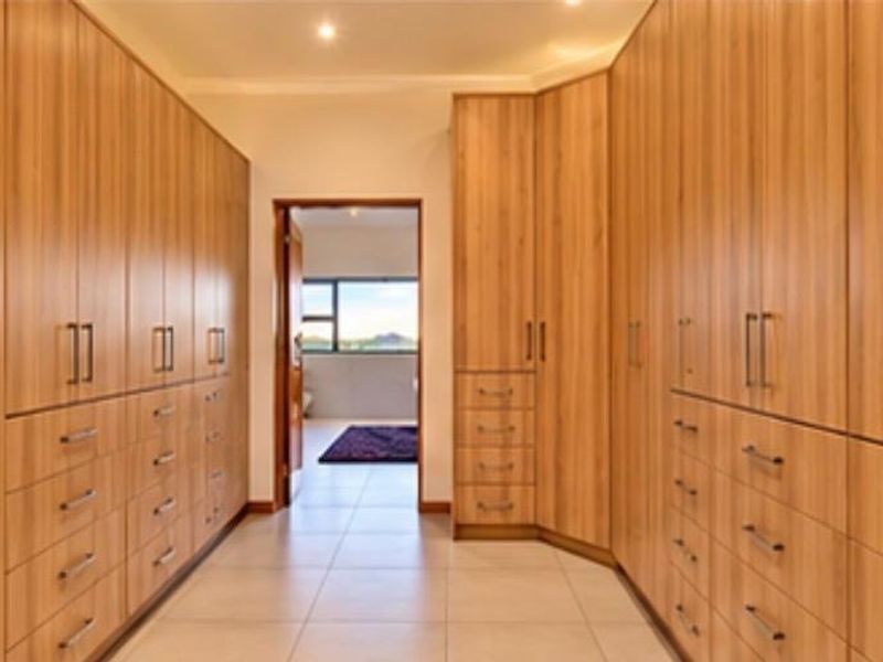 A spacious walk-in dressing area featuring extensive floor-to-ceiling built-in wooden cabinetry with ample storage and modern tiled flooring.
