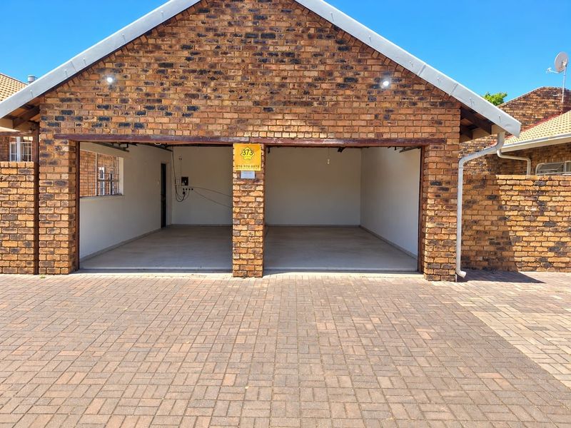 A double garage with a face brick exterior and paved driveway, currently lacking garage doors.