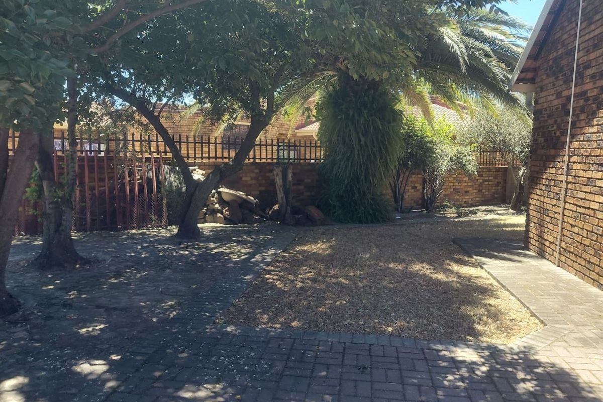 A rear garden area featuring brick boundary walls, paved sections, and established trees, providing a private outdoor space.
