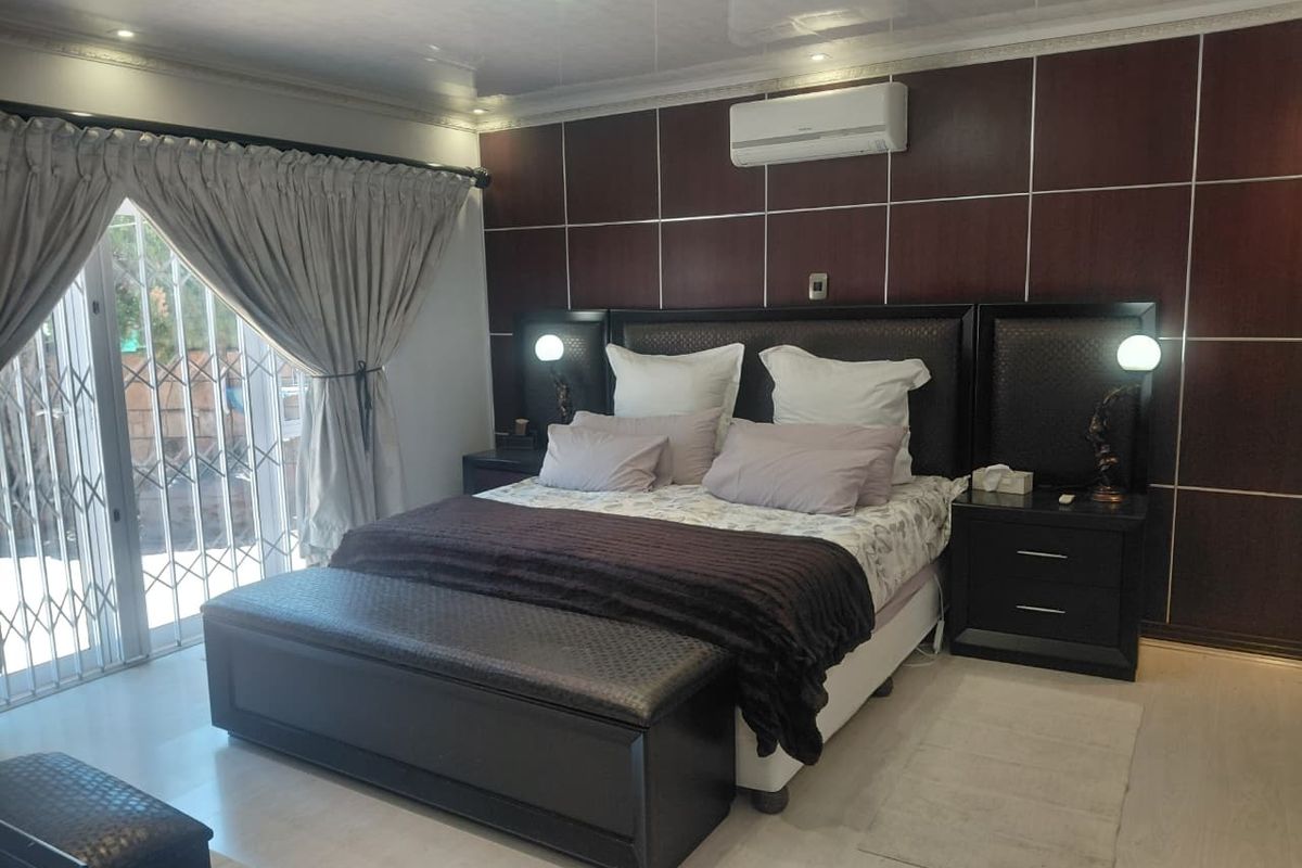 A well-maintained bedroom featuring dark wood-look wall paneling, laminate flooring, a split-system air conditioner, and sliding glass doors with security gates leading outdoors.