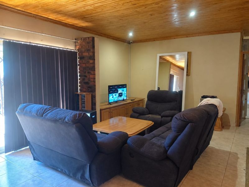 A living room featuring a timber tongue and groove ceiling, tiled flooring, and an exposed brick feature pillar.