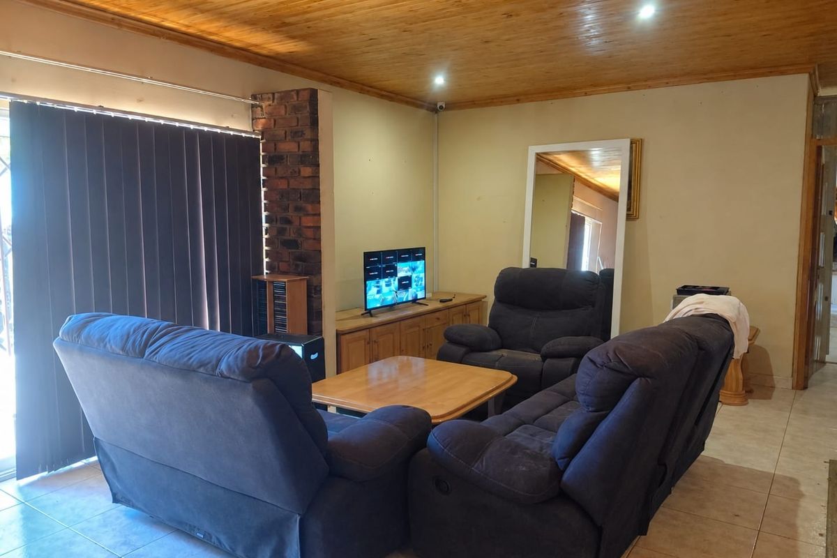 A living room featuring a timber tongue and groove ceiling, tiled flooring, and an exposed brick feature pillar.