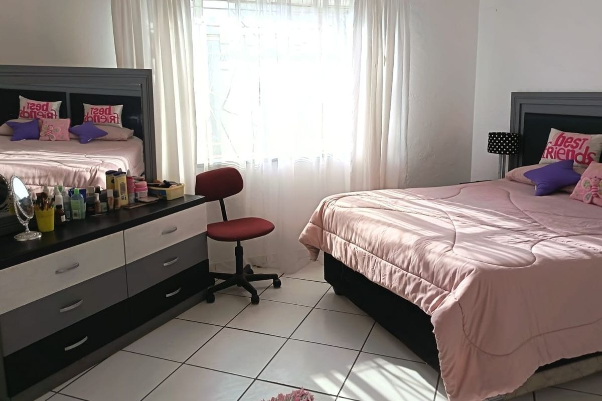 A bedroom featuring tiled flooring and a window fitted with security bars, providing natural light.