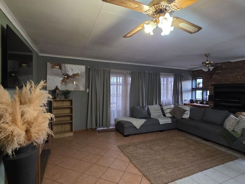 Spacious living room featuring a brick fireplace, ceiling fans, and tiled flooring with direct access to the outdoor area through sliding glass doors.