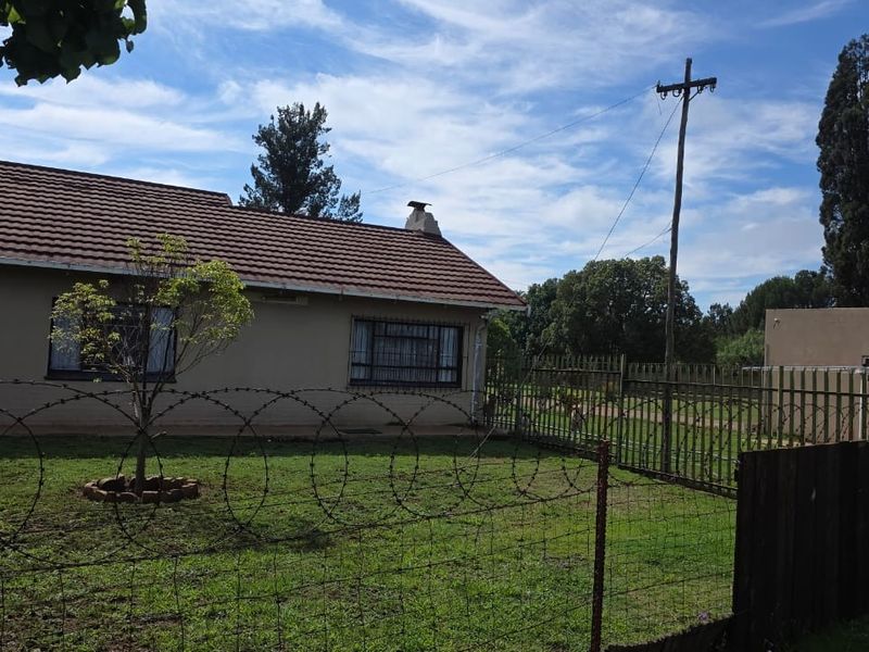 Rear view of the property featuring a tiled roof, chimney, and security fencing with razor wire surrounding the garden area.