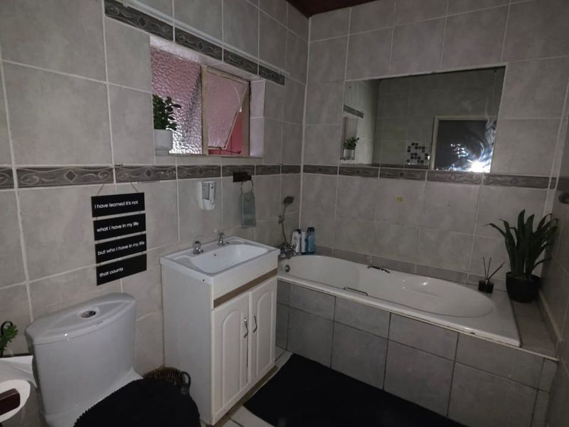 A functional bathroom featuring a built-in bathtub, vanity cabinet with basin, and full-height wall tiling.