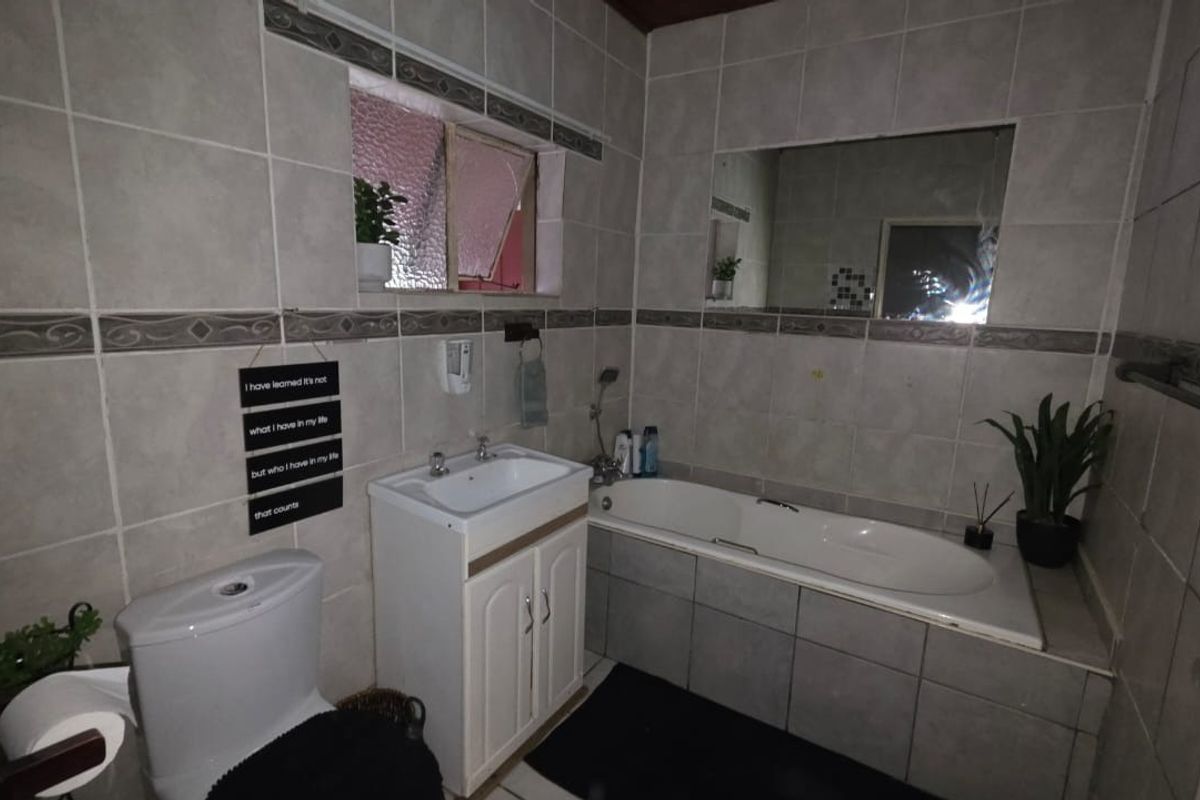 A functional bathroom featuring a built-in bathtub, vanity cabinet with basin, and full-height wall tiling.
