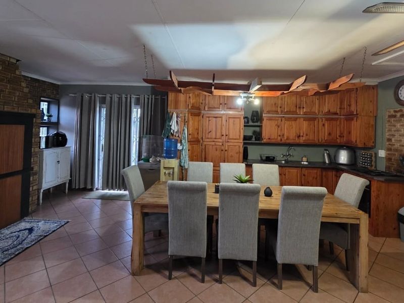 Open plan living and dining area featuring a brick fireplace, tiled floors, and wooden kitchen cabinetry with a central dining space.