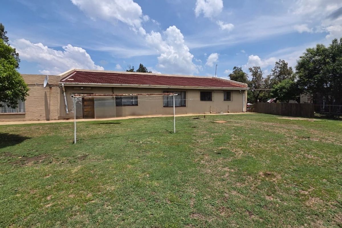 Rear view of the property featuring a spacious lawn, brick exterior walls, and a tiled roof, providing ample outdoor space.