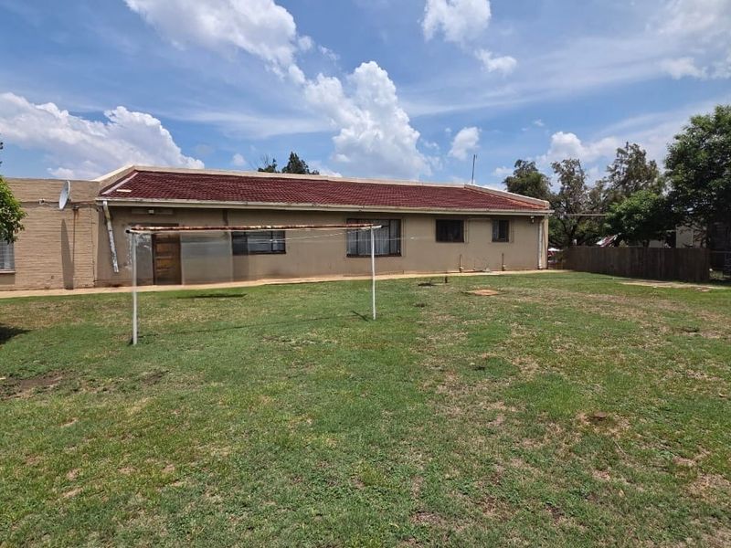 Rear view of the property featuring a spacious lawn, brick exterior walls, and a tiled roof, providing ample outdoor space.