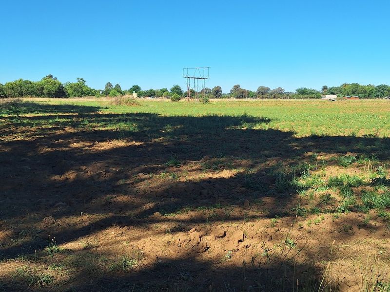 A wide, open plot of land featuring a metal water tower structure and natural vegetation, suitable for agricultural or development purposes.