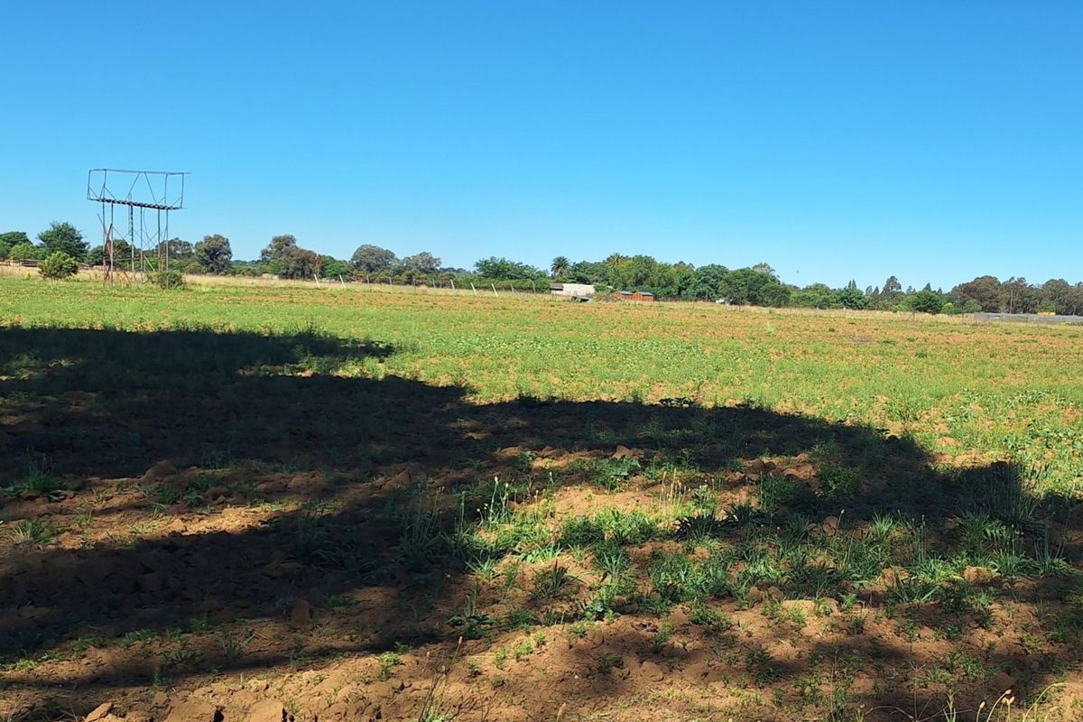 Expansive open land area on the small holding, featuring natural terrain and a metal water tower structure under a clear sky.