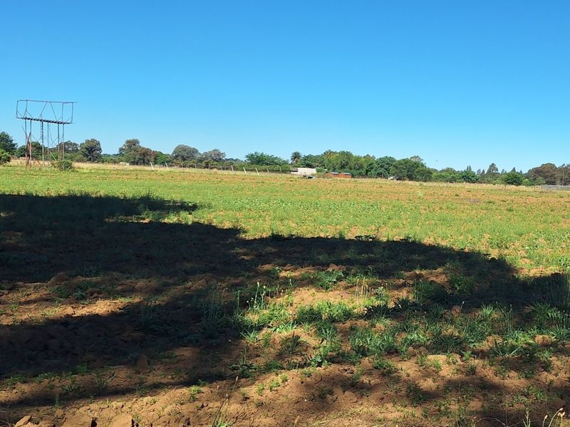 Expansive open land area on the small holding, featuring natural terrain and a metal water tower structure under a clear sky.