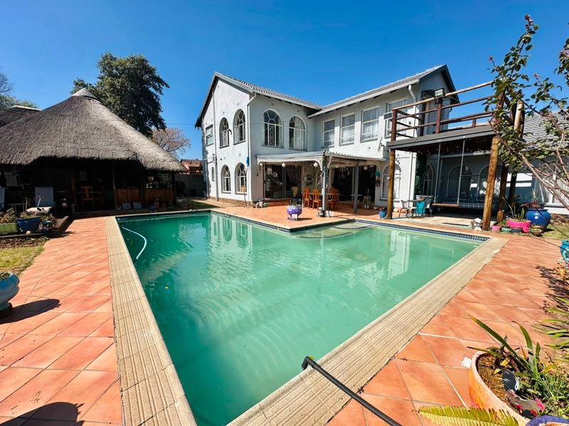 Rear exterior view featuring a swimming pool, tiled patio area, and a separate thatched lapa structure set against the main house.