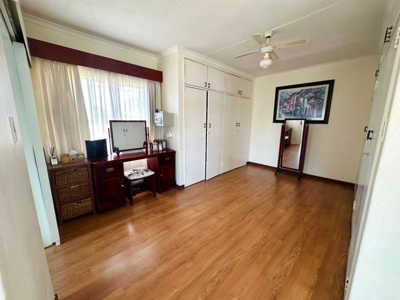 A well-maintained bedroom featuring laminate flooring, built-in cupboards, and a ceiling fan, offering a clean and functional living space.