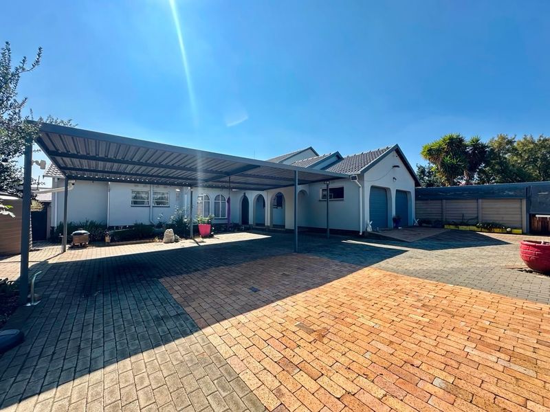 Front exterior view of the house featuring a large metal carport, paved driveway, and double garage access.